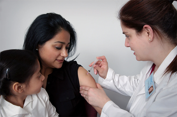 doctor administering a shot to a mom while her daughter watches